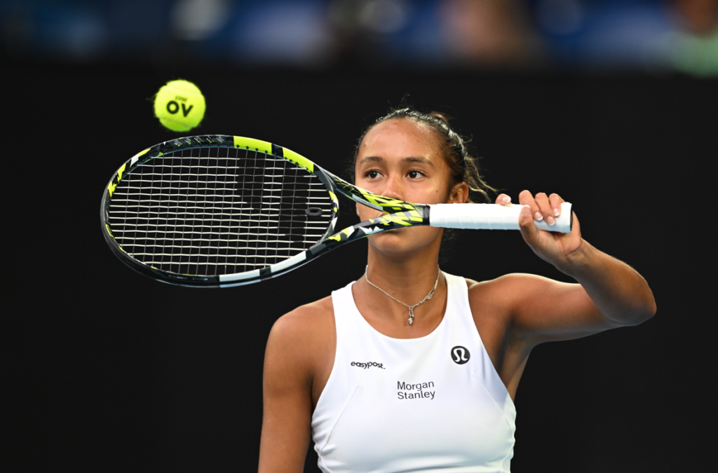 Leylah Fernandez holds the racket up in front of her face and bounces a ball.